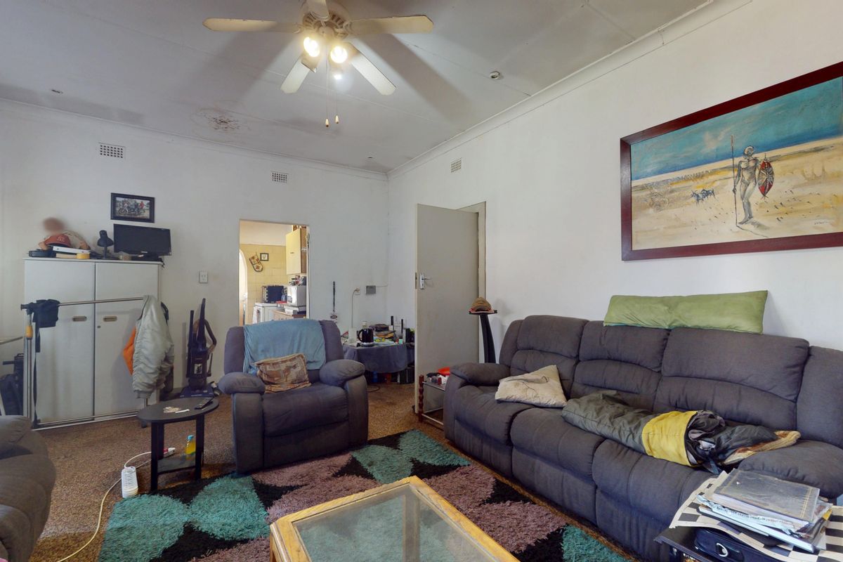 A living room featuring a ceiling fan and original cornicing, showing signs of wear on the ceiling and flooring.