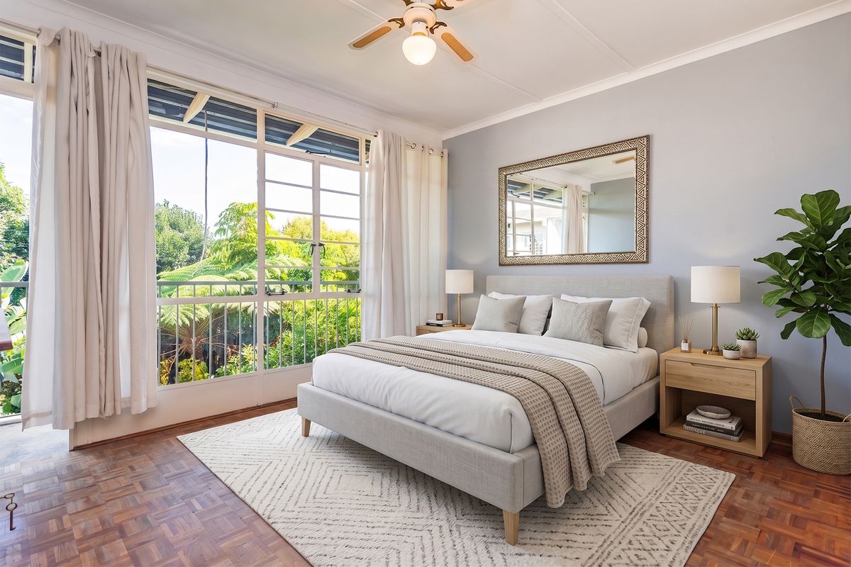 A bright and airy bedroom featuring classic parquet flooring, a ceiling fan, and large windows providing natural light and access to a balcony.