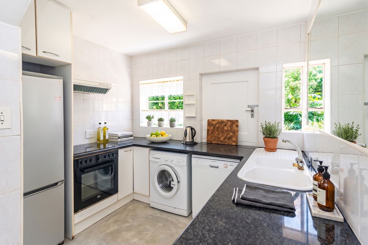 A functional kitchen featuring dark granite countertops, white cabinetry, tiled walls, and integrated appliances including an oven and extractor fan.