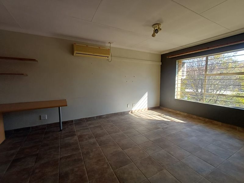 An empty living area featuring tiled flooring, a wall-mounted air conditioning unit, built-in desk space, and large windows with security bars.