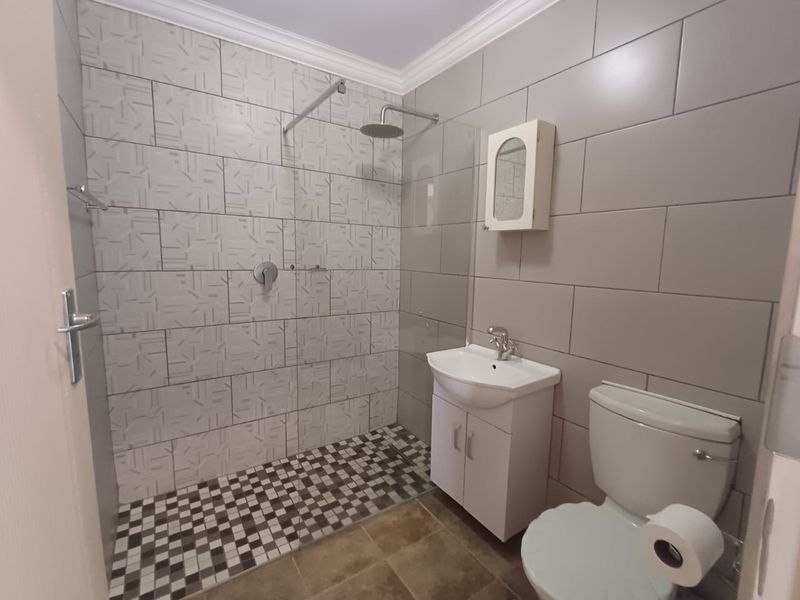 Modern bathroom featuring a walk-in shower with a rain shower head, glass screen, vanity cabinet with basin, and neutral wall and floor tiling.