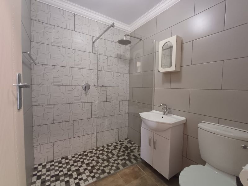 Modern bathroom featuring a walk-in shower with a rain shower head, glass screen, vanity cabinet, and neutral wall tiling.