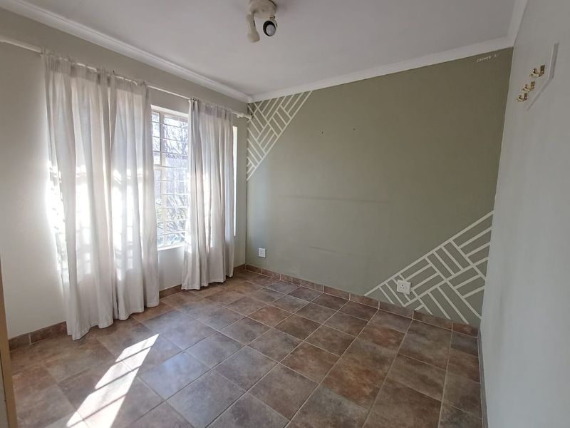 An empty bedroom featuring tiled flooring, security bars on the window, and a decorative painted accent wall.