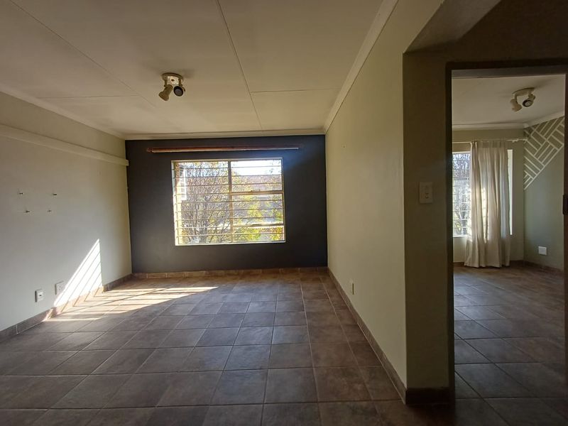 An empty living room featuring tiled flooring, a dark accent wall, and security bars on the window, offering a blank canvas for personalization.
