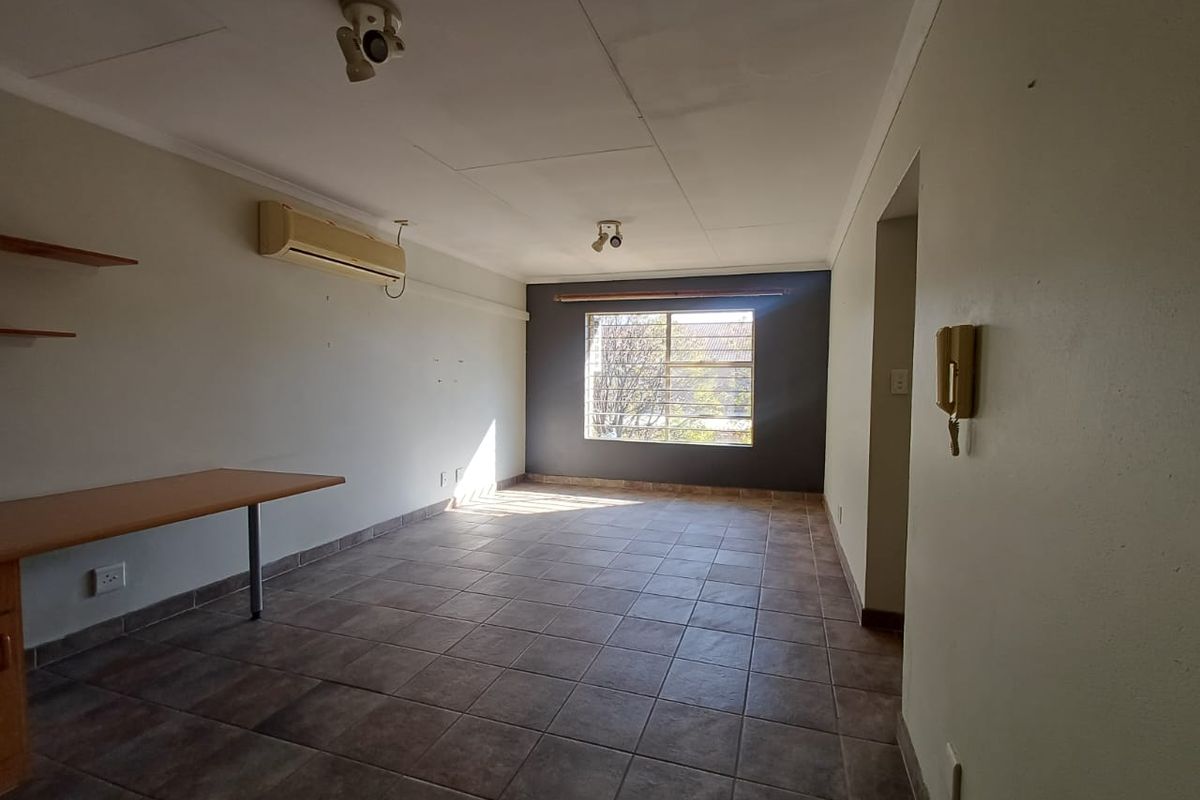 An empty living area featuring tiled flooring, a wall-mounted air conditioning unit, and a built-in desk, offering a functional space ready for personalization.