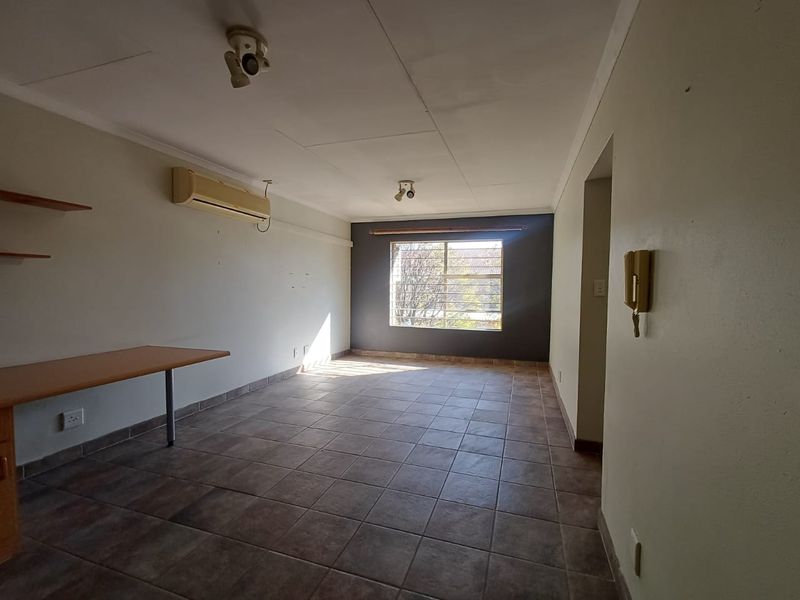 An empty living area featuring tiled flooring, a wall-mounted air conditioning unit, and a built-in desk, offering a functional space ready for personalization.