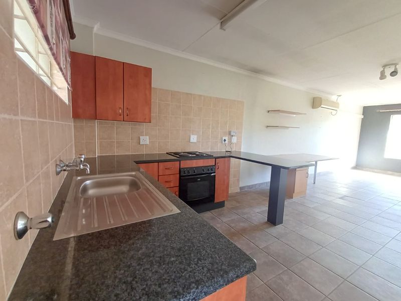 Open-plan kitchen and living area featuring granite countertops, built-in oven and hob, tiled flooring, and wall-mounted air conditioning unit.