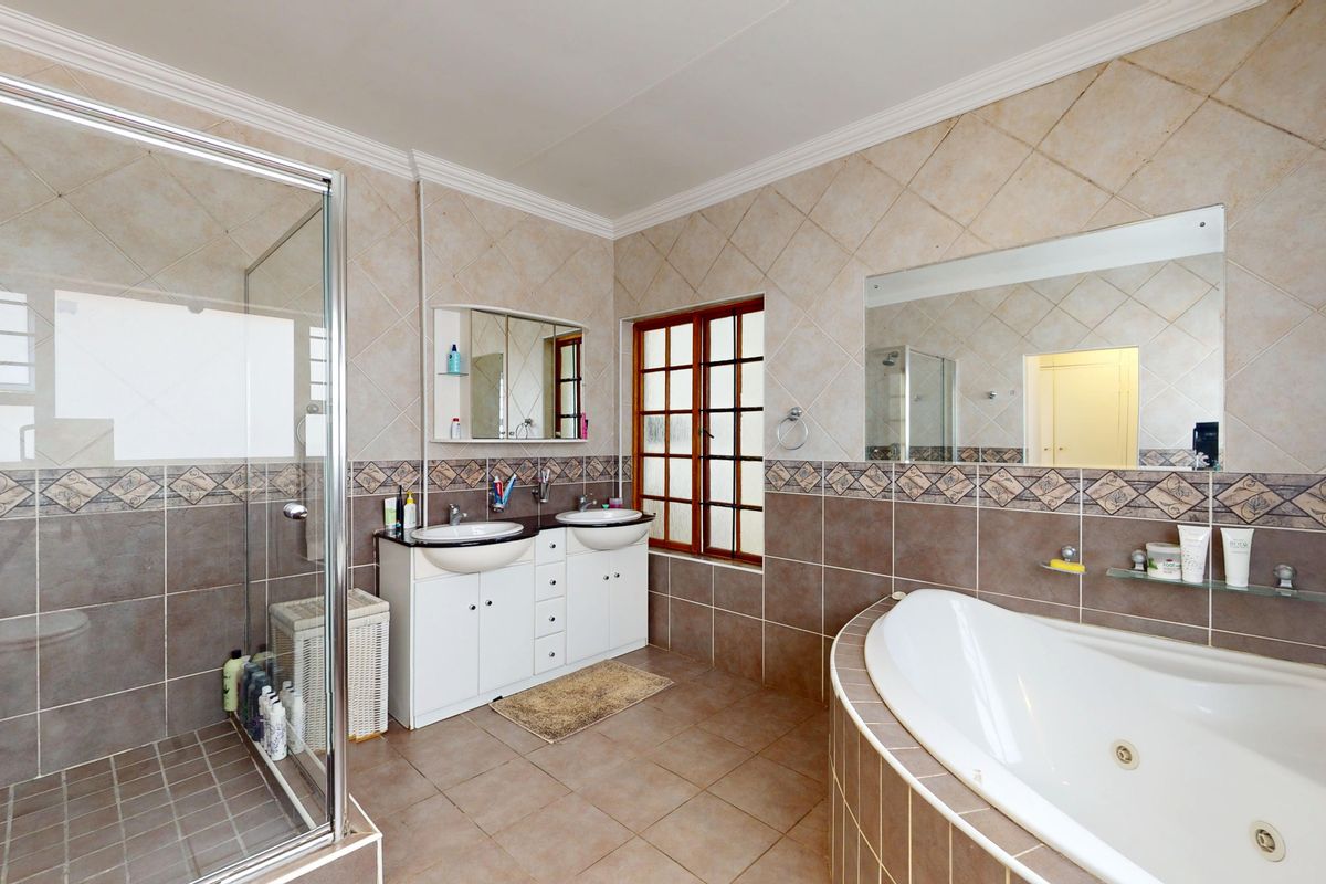 Spacious bathroom featuring a double vanity, a built-in corner bathtub, and a separate glass-enclosed shower with neutral tiled finishes.