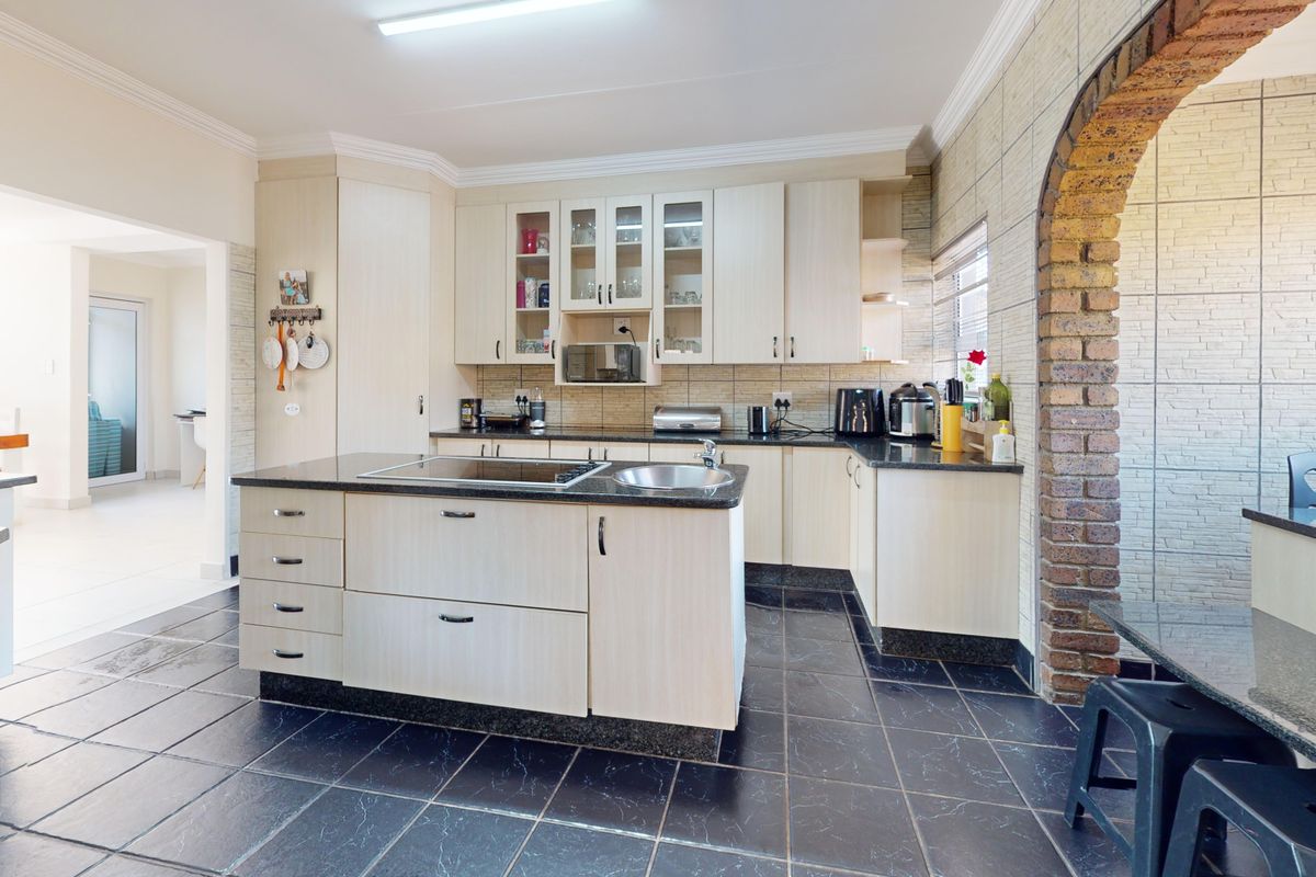 A functional kitchen featuring light wood cabinetry, a central island with a built-in hob, stone countertops, and a distinctive brick archway detail.