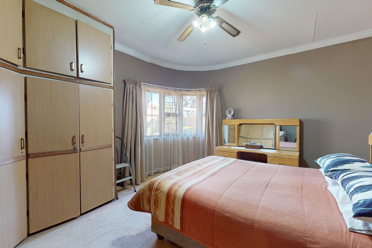 A bedroom featuring built-in wooden cupboards, a ceiling fan, and a bay window with natural light.