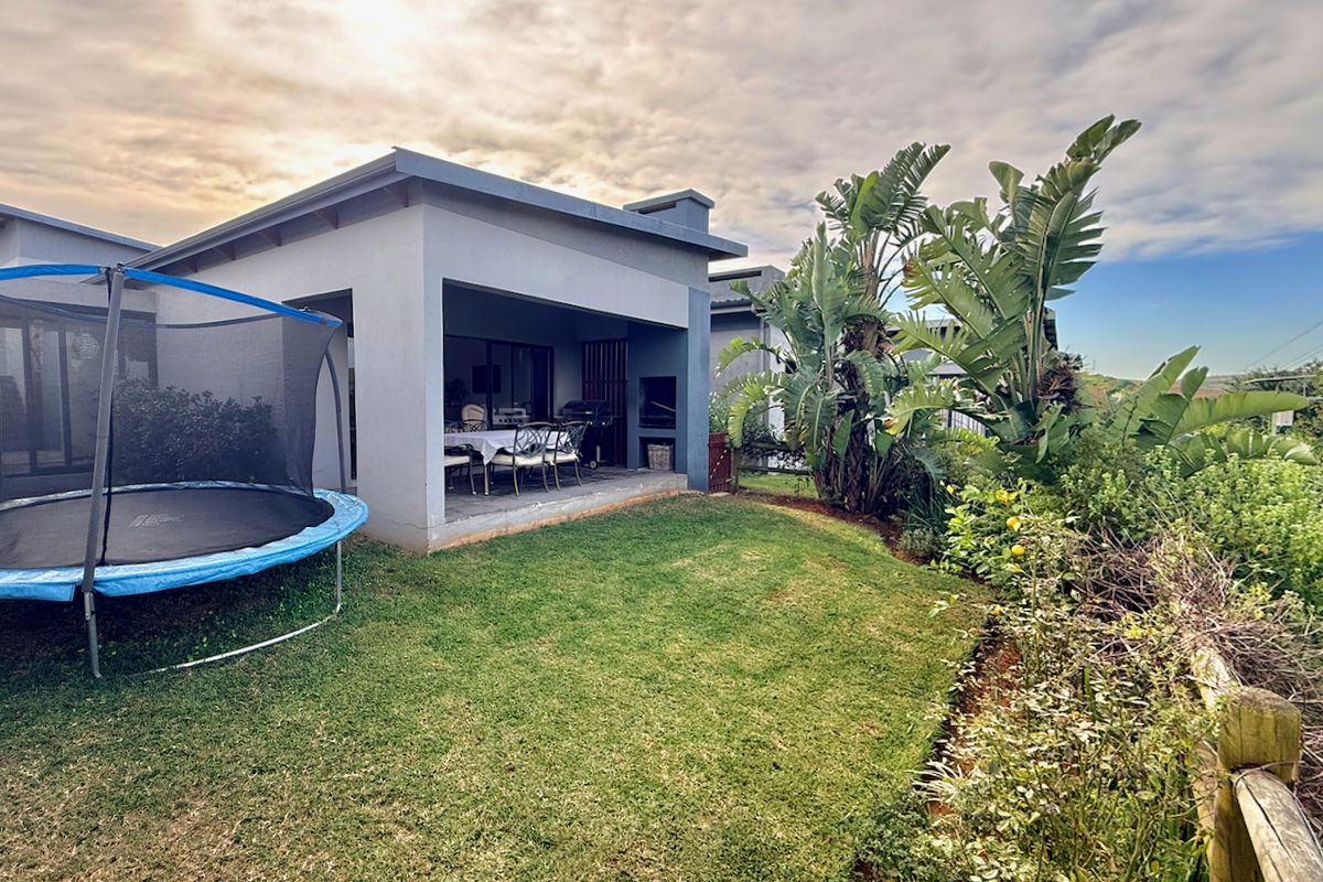 Rear view of the property featuring a covered patio with a built-in braai, overlooking a private garden area.