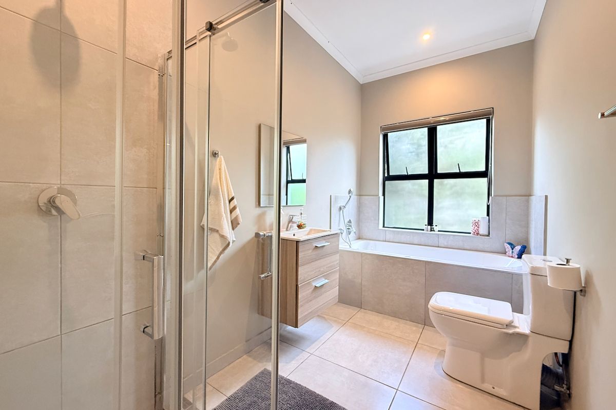 Modern bathroom featuring a glass-enclosed shower, wall-mounted vanity, built-in bathtub, and neutral tiled finishes throughout.