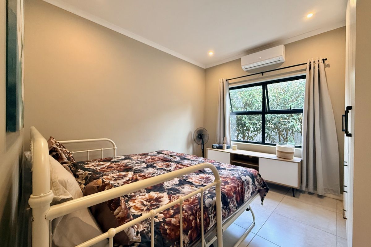 A well-maintained bedroom featuring tiled flooring, recessed downlighting, a split-system air conditioner, and a built-in cupboard.