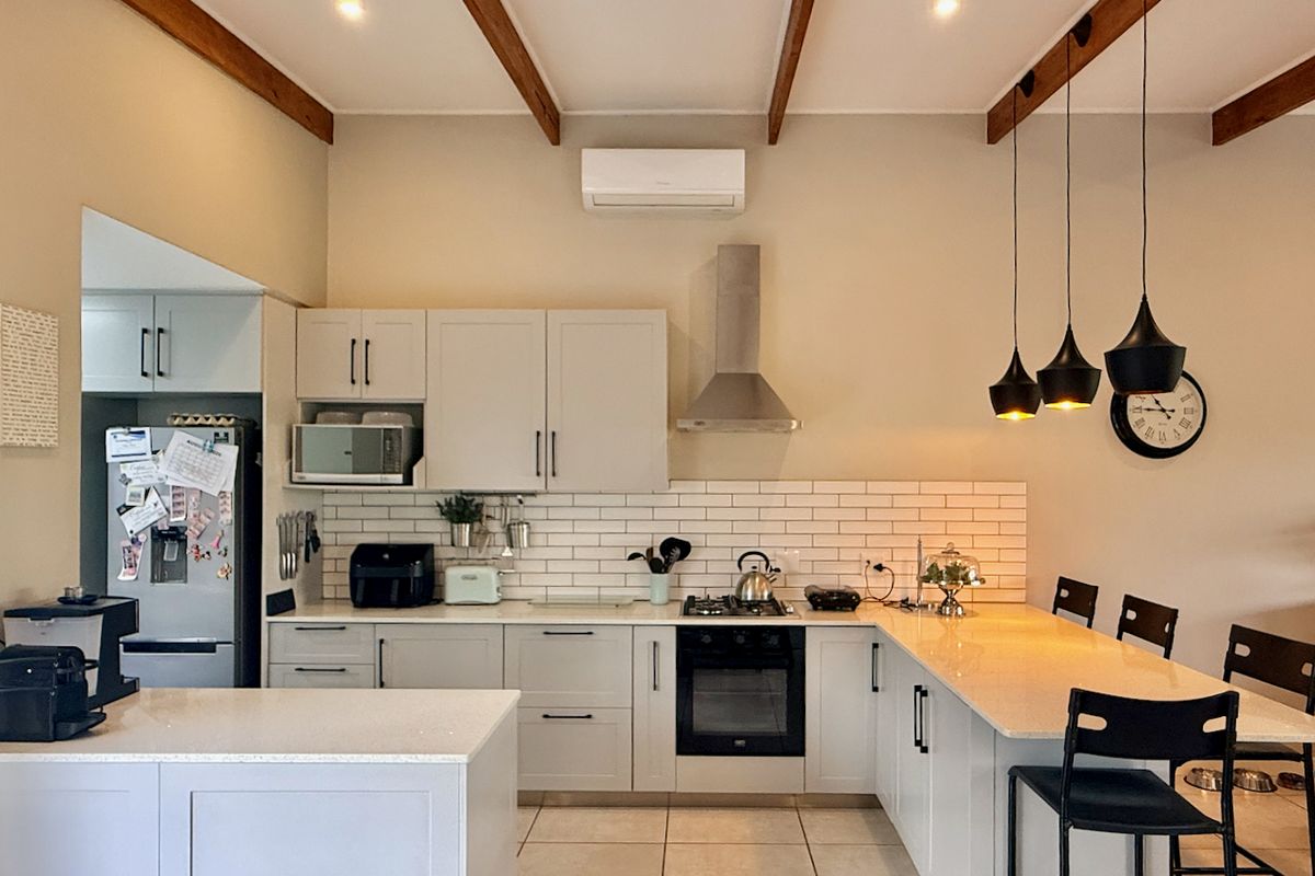 Modern kitchen featuring shaker-style cabinetry, stone countertops, subway tile backsplash, built-in oven, gas hob, and exposed timber ceiling beams.