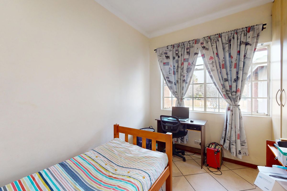 A functional bedroom featuring tiled flooring, a built-in wardrobe, and a window with security bars, providing a practical living space.