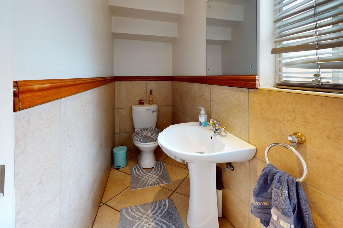 A compact guest bathroom featuring a pedestal sink, toilet, and neutral wall tiling with a wooden dado rail finish.