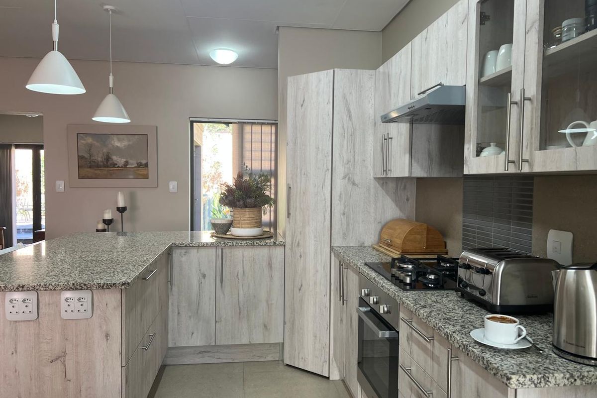 Modern kitchen featuring light wood-grain cabinetry, granite countertops, built-in gas hob, oven, and extractor fan, complemented by stylish pendant lighting.