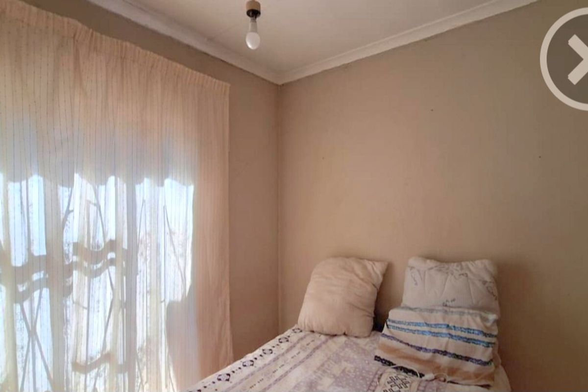 A bedroom featuring neutral wall paint, cove cornicing, and a large window with curtains. The room shows signs of wear and requires cosmetic updates.