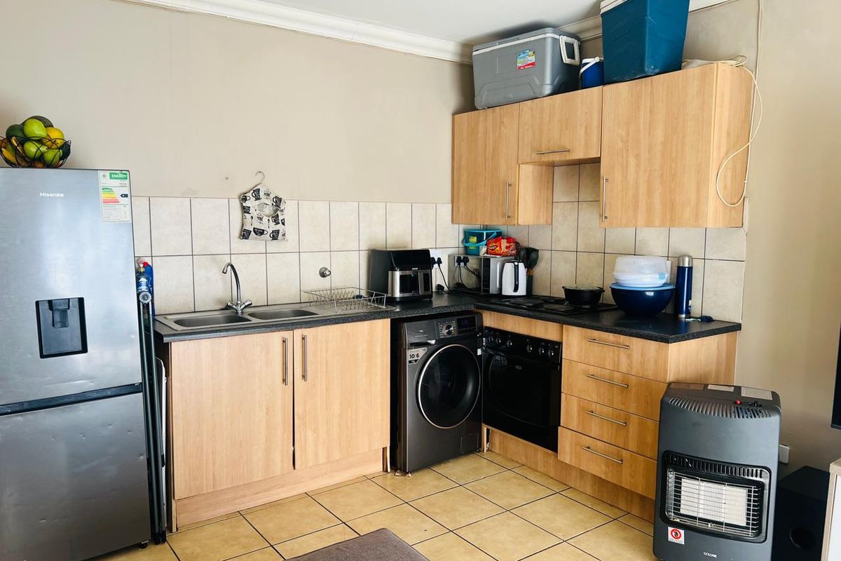 Compact kitchen featuring laminate cabinetry, tiled backsplash, built-in oven, hob, and integrated washing machine with tiled flooring.