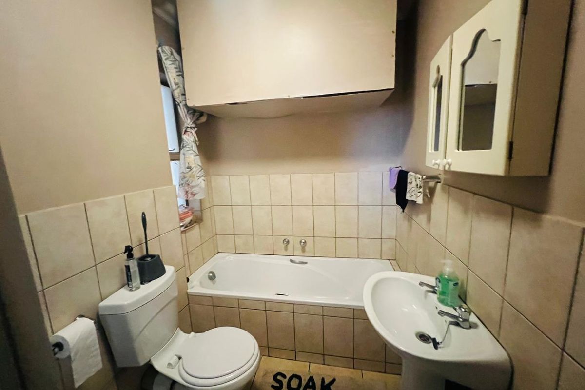 A functional bathroom featuring a standard bathtub, pedestal basin, toilet, and wall-mounted medicine cabinet with neutral tiled splashbacks.