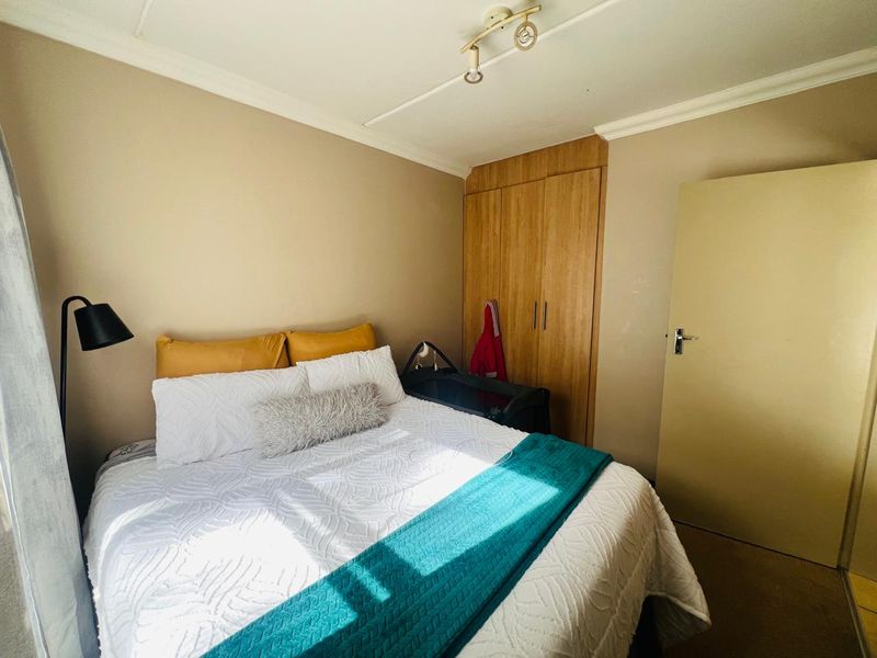 A functional bedroom featuring a built-in wooden wardrobe, neutral wall finishes, and overhead lighting, providing a comfortable and practical living space.