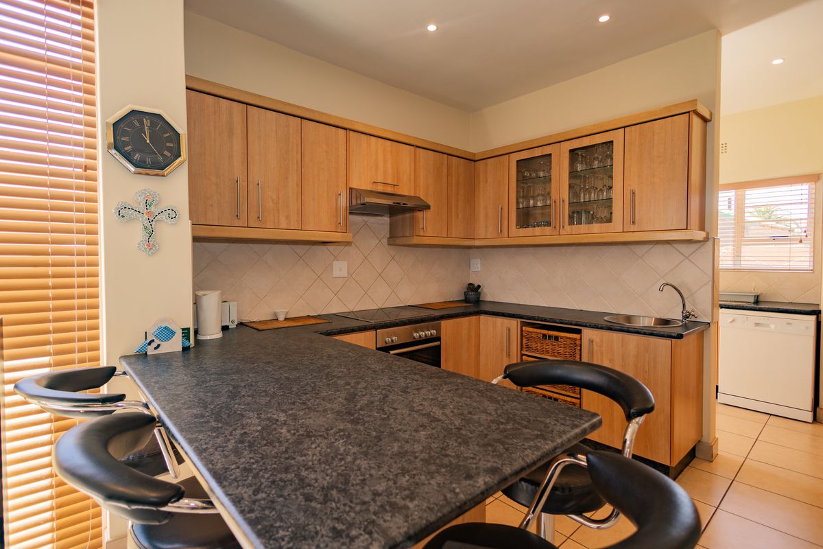 A functional kitchen featuring light wood cabinetry, dark laminate countertops, a built-in oven with hob, and a breakfast bar area.