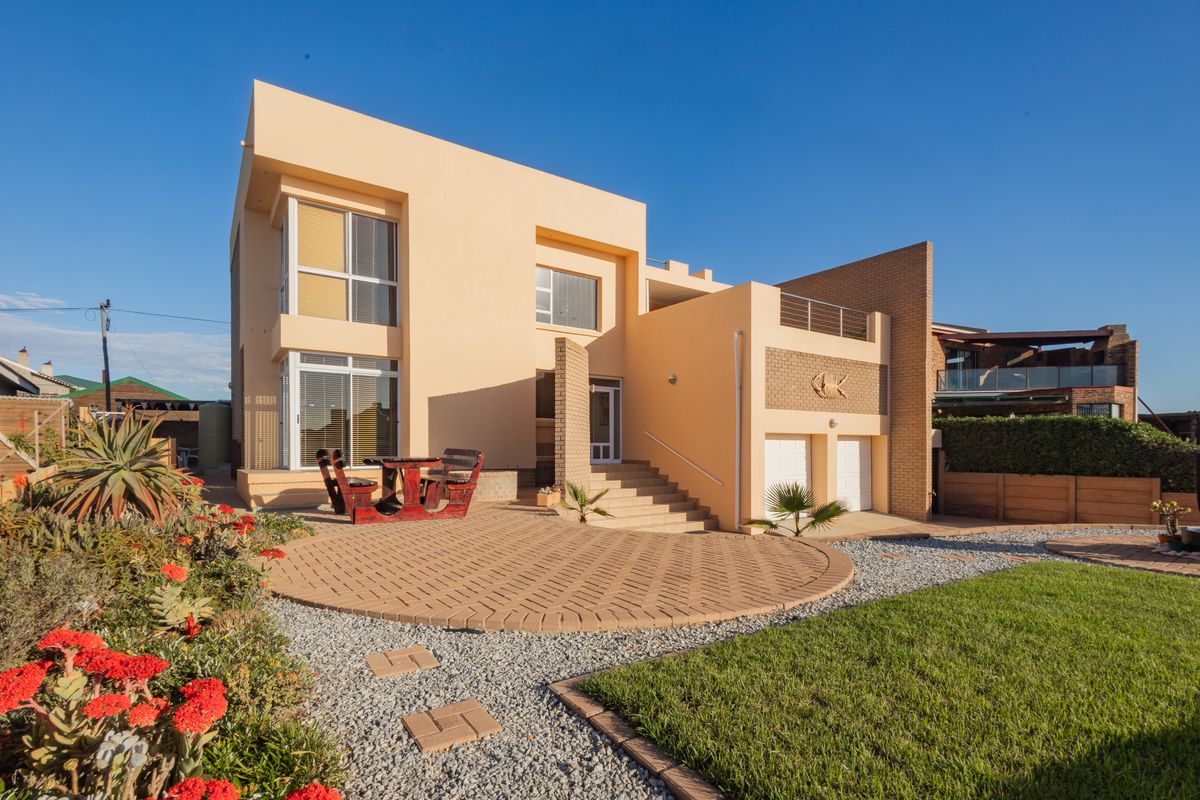 Rear view of a modern multi-level house featuring a paved patio area, landscaped garden, and integrated double garage.