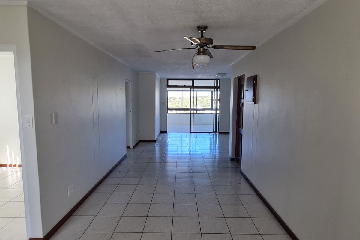 An empty, open-plan living area featuring tiled flooring, a ceiling fan, and access to a balcony through sliding glass doors.