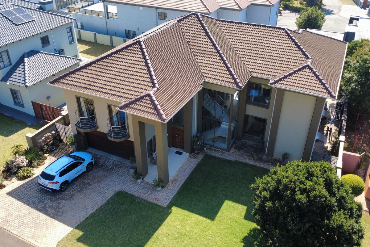 Aerial view of a modern two-story residential property featuring a tiled roof, paved driveway, double garage, and well-maintained garden.