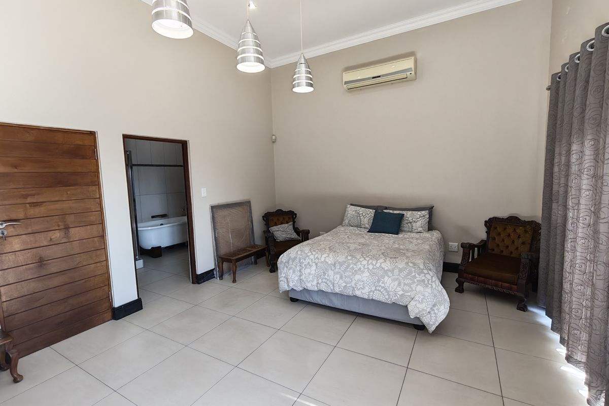 Spacious bedroom featuring tiled flooring, air conditioning, and pendant lighting, with direct access to an en-suite bathroom.