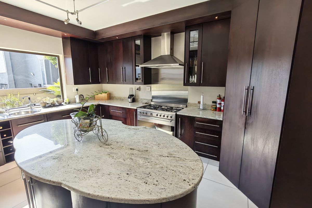 Modern kitchen featuring dark wood cabinetry, granite countertops, a central island, and stainless steel appliances including a gas stove and extractor fan.