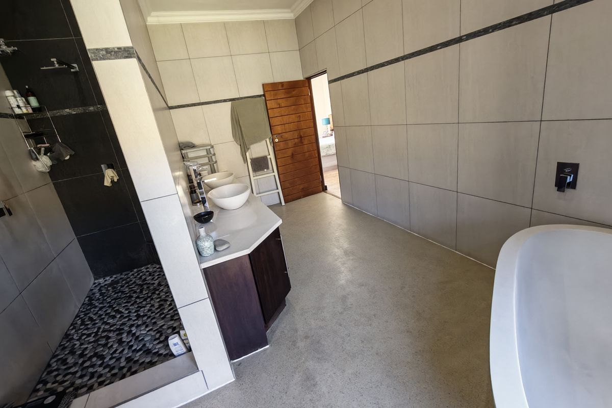 Spacious modern bathroom featuring a walk-in shower with pebble flooring, a double vanity with vessel sinks, and a contemporary freestanding bathtub.