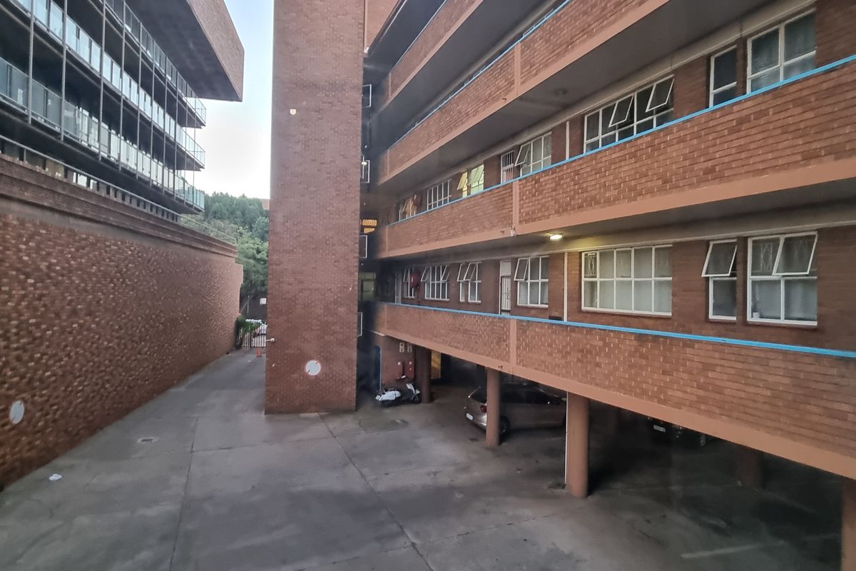 Exterior view of a multi-story brick apartment building featuring covered parking and residential units with casement windows.