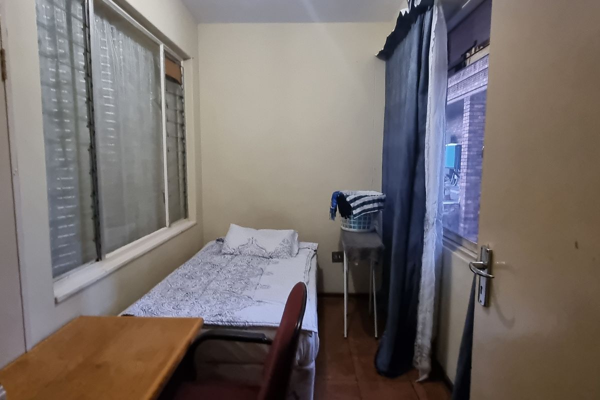 A compact bedroom featuring tiled flooring and louvered windows, offering a functional space that would benefit from cosmetic updates and fresh paint.