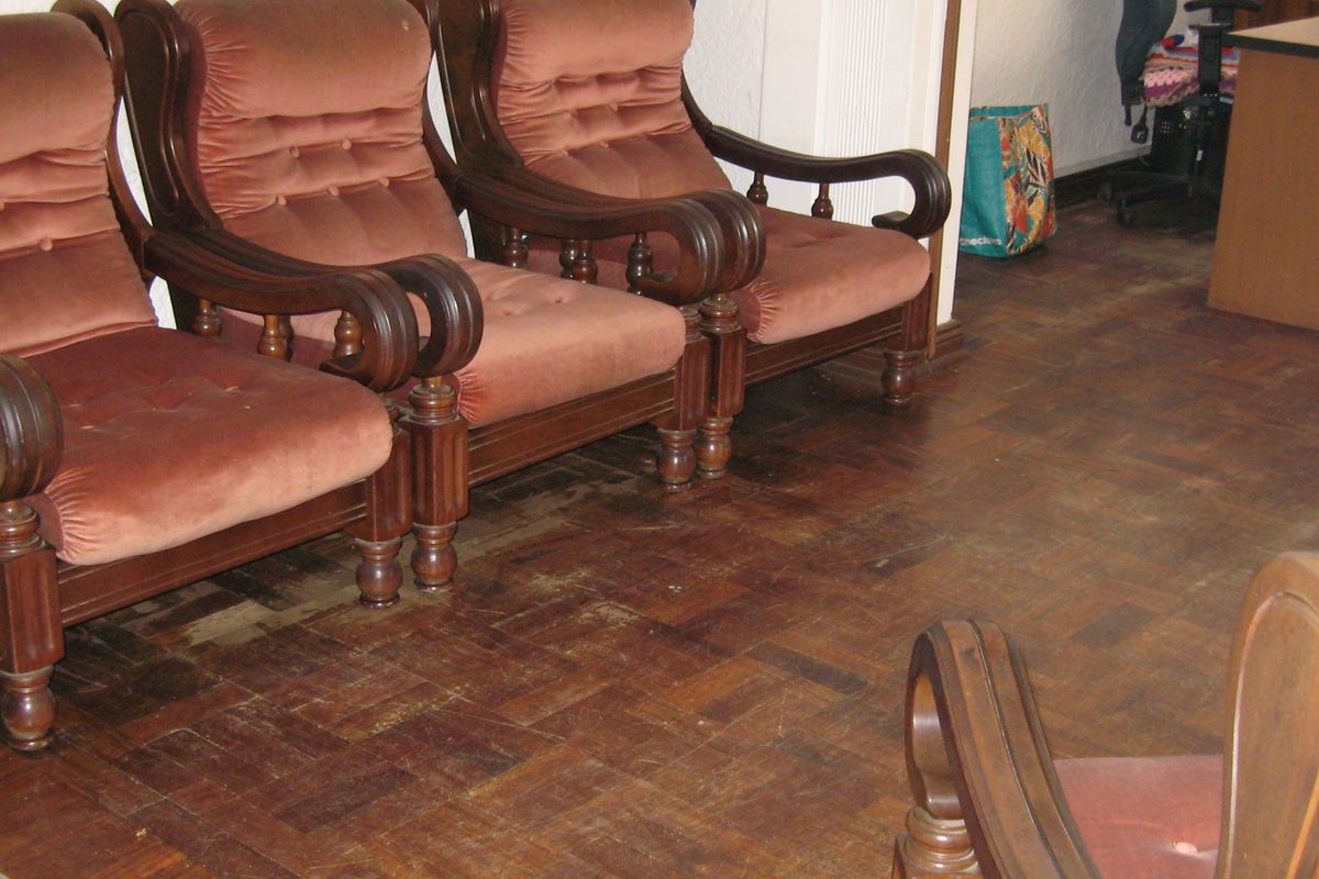 A living area featuring traditional parquet wood flooring, showing signs of wear and requiring refinishing to restore its original character.