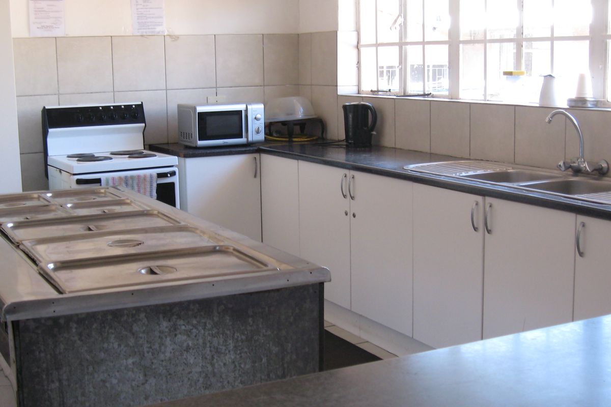 Functional kitchen featuring white cabinetry, tiled backsplash, stainless steel sink, and a freestanding stove, offering a practical layout for food preparation.