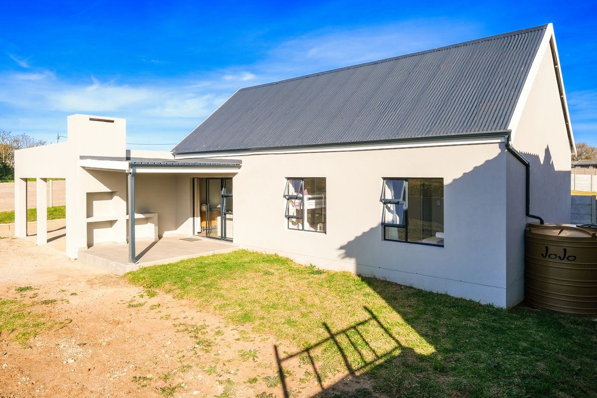 Rear view of the townhouse featuring a covered patio with a built-in braai, corrugated metal roof, and a water storage tank.