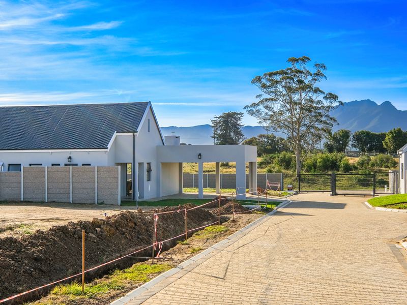 A modern townhouse exterior featuring a pitched roof, covered carport, and paved driveway, set within a developing residential estate with mountain views.