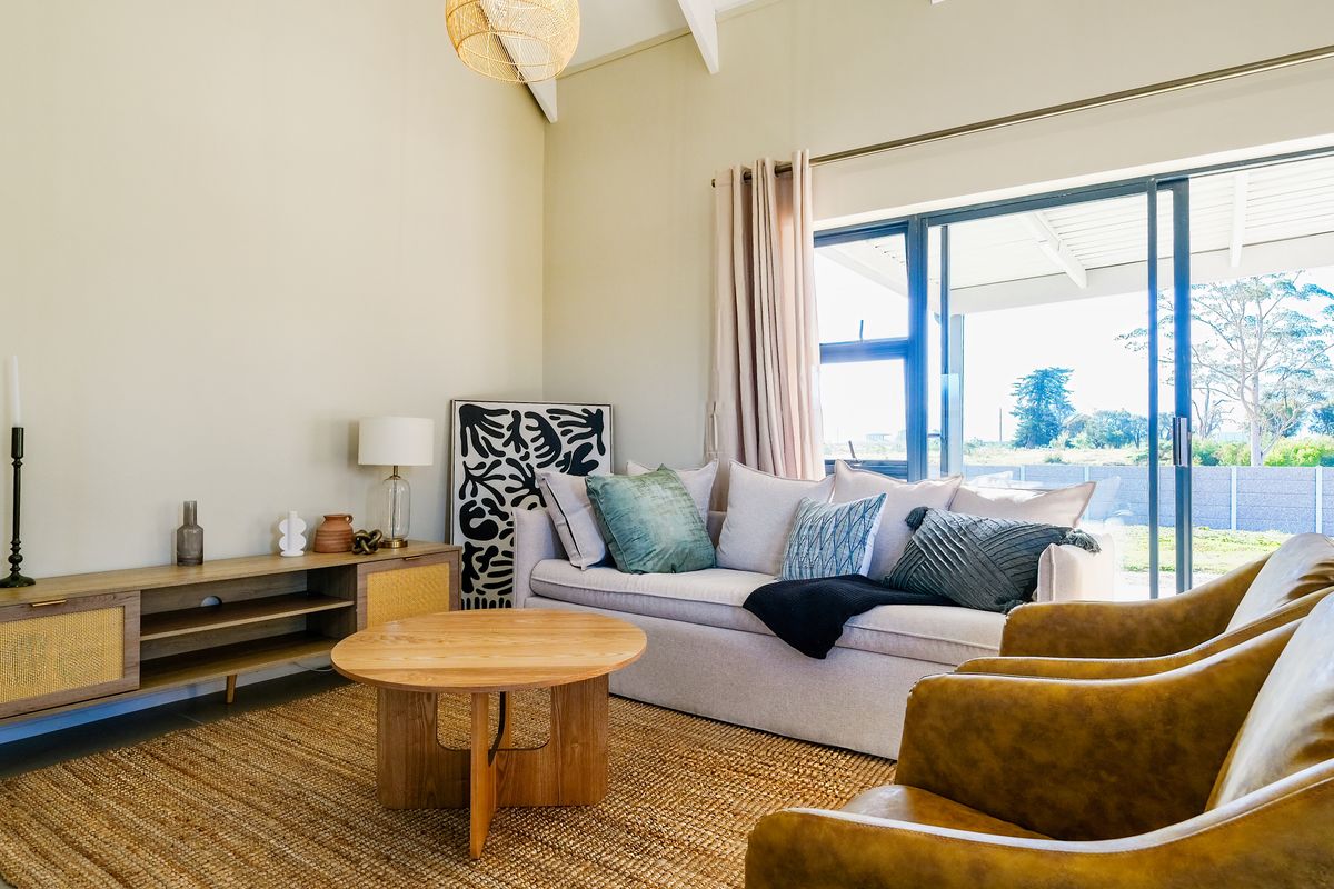 A bright living room featuring high vaulted ceilings, tiled flooring, and large sliding glass doors that open onto a covered patio area.