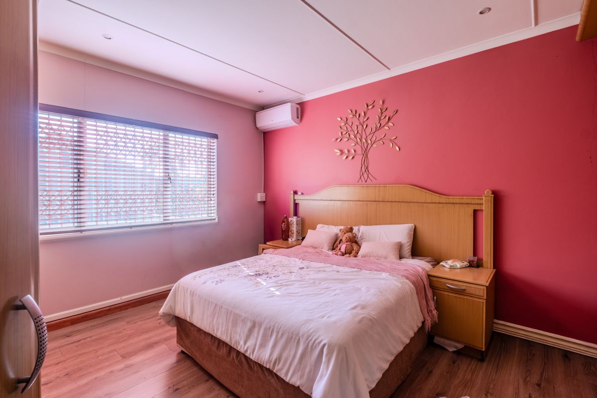 A bedroom featuring laminate flooring, a split-system air conditioner, and venetian blinds, with a bold accent wall.