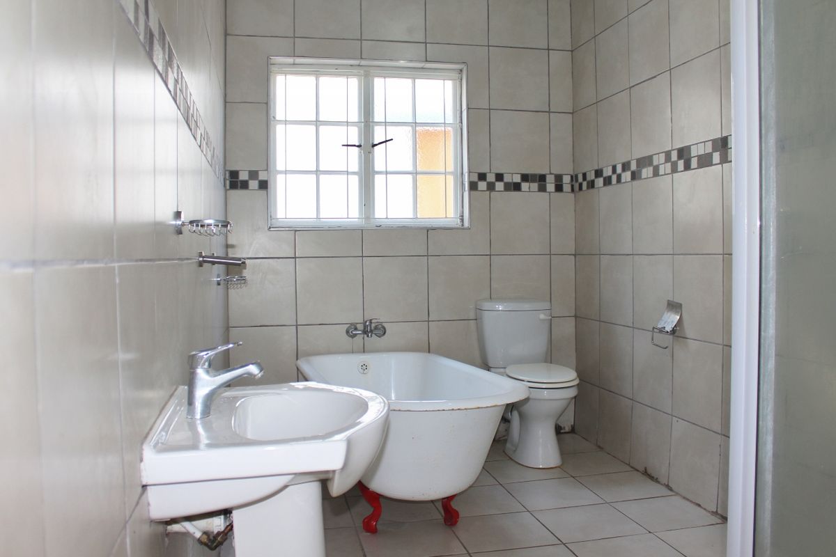 A dated bathroom featuring a pedestal basin, a vintage-style clawfoot bathtub, and a standard toilet, finished with neutral wall and floor tiles.