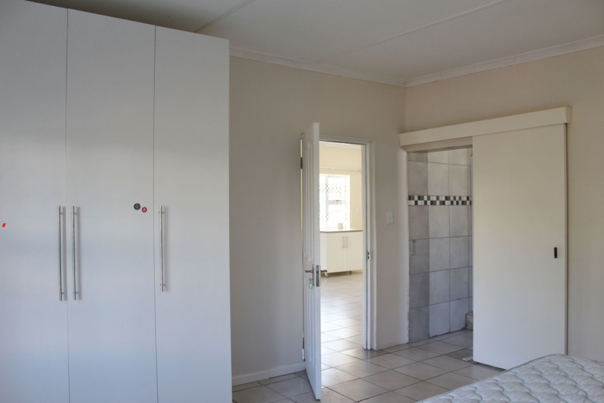 A spacious bedroom featuring built-in cupboards, tiled flooring, and direct access to an adjoining room.