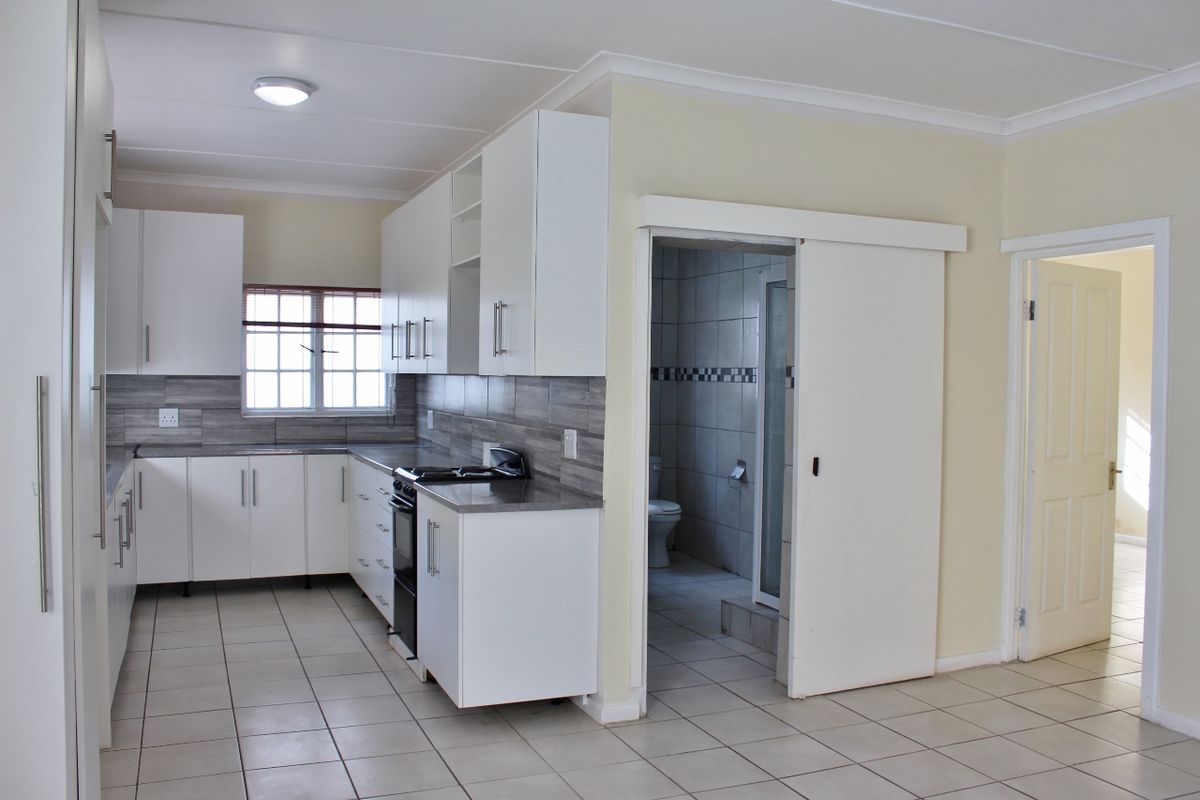 A clean, functional kitchen featuring white cabinetry, grey laminate countertops, tiled backsplash, and direct access to an adjacent bathroom.