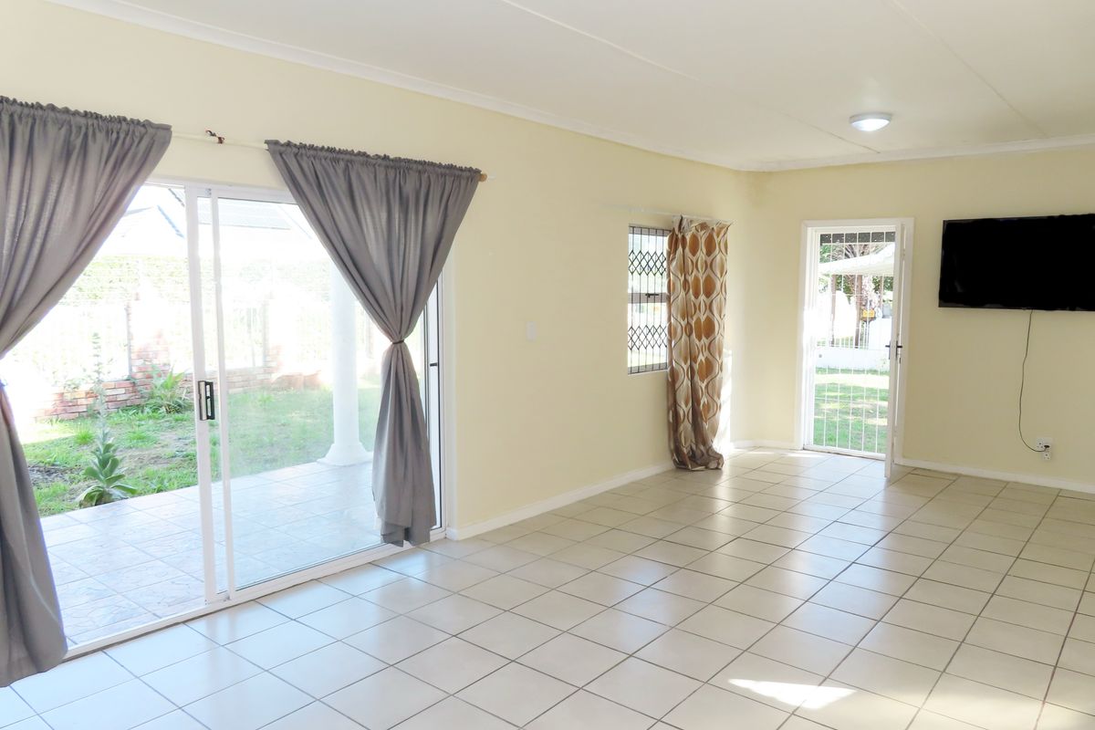 A bright, open-plan living area featuring neutral tiled flooring, a sliding glass door leading to the patio, and a security gate at the entrance.
