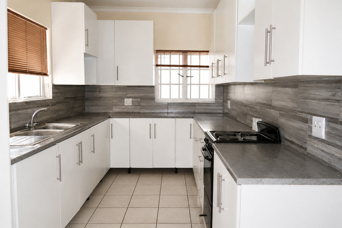 A clean, functional kitchen featuring white cabinetry, grey stone-look countertops, tiled backsplash, and integrated electric cooking appliances.