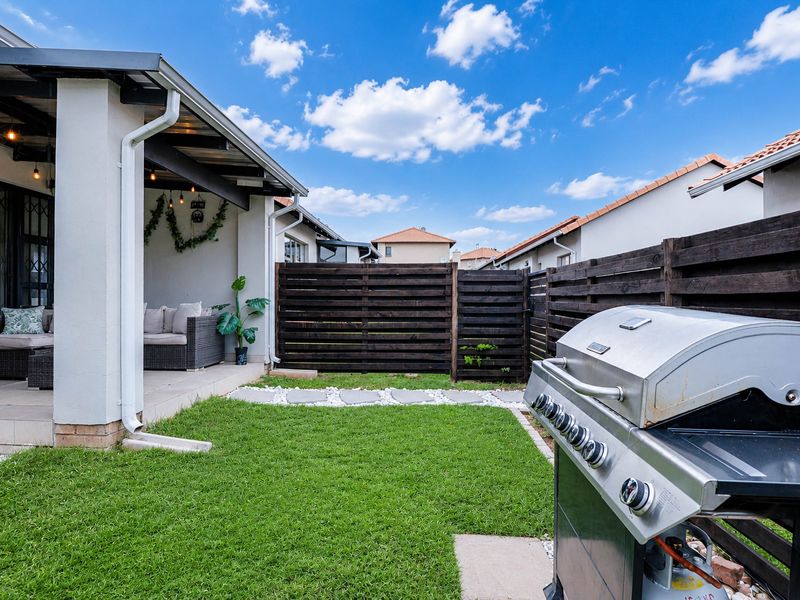 A well-maintained rear garden featuring a covered patio area, neat lawn, and timber slat privacy fencing.