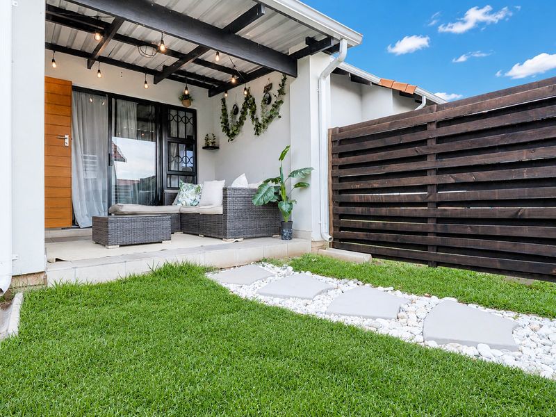 A well-maintained covered patio featuring a timber pergola and privacy screen, leading out to a landscaped garden with a stone paver pathway.