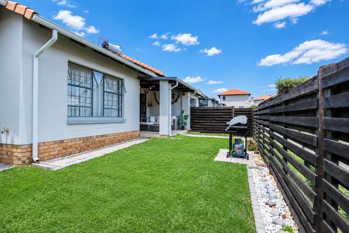 A well-maintained rear garden featuring a manicured lawn, timber slat fencing, and a covered patio area with a solar water heater installed on the roof.