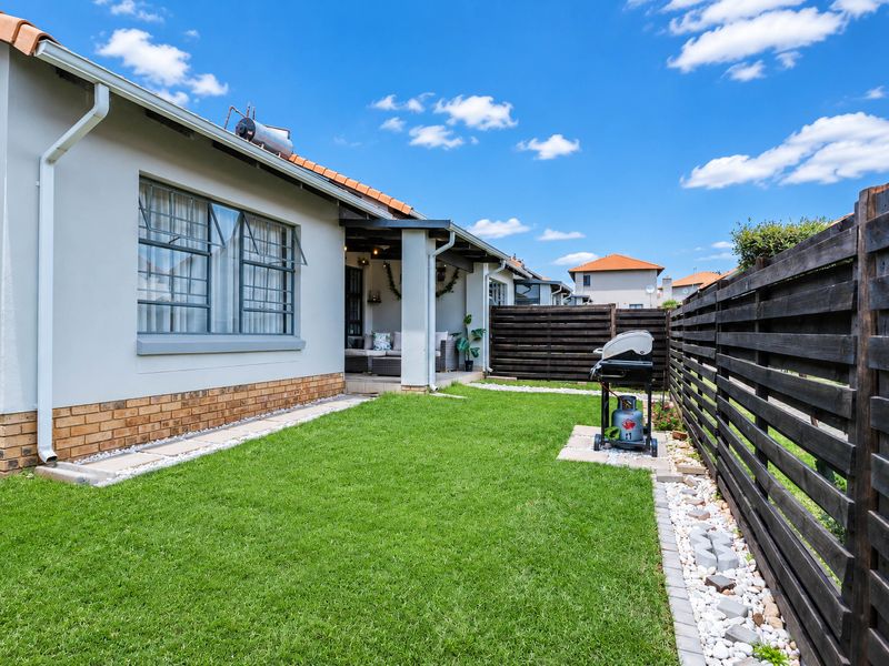 A well-maintained rear garden featuring a manicured lawn, timber slat fencing, and a covered patio area with a solar water heater installed on the roof.