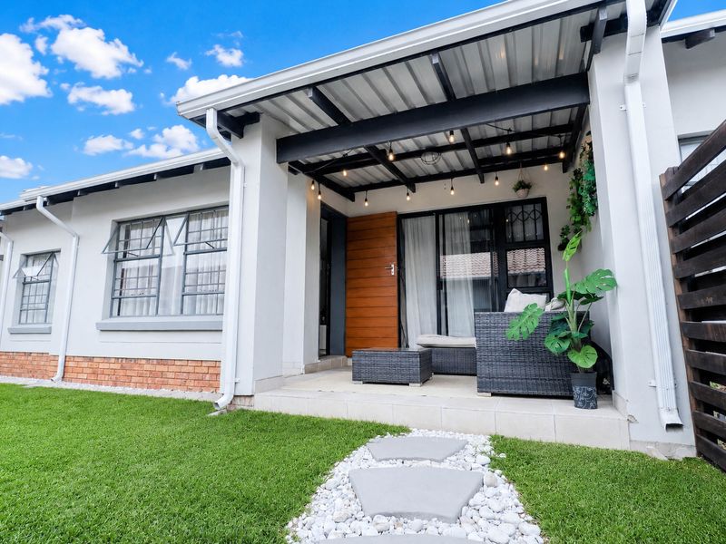 A well-maintained covered patio area featuring tiled flooring, exposed beams, and direct access to the garden through a modern sliding glass door.